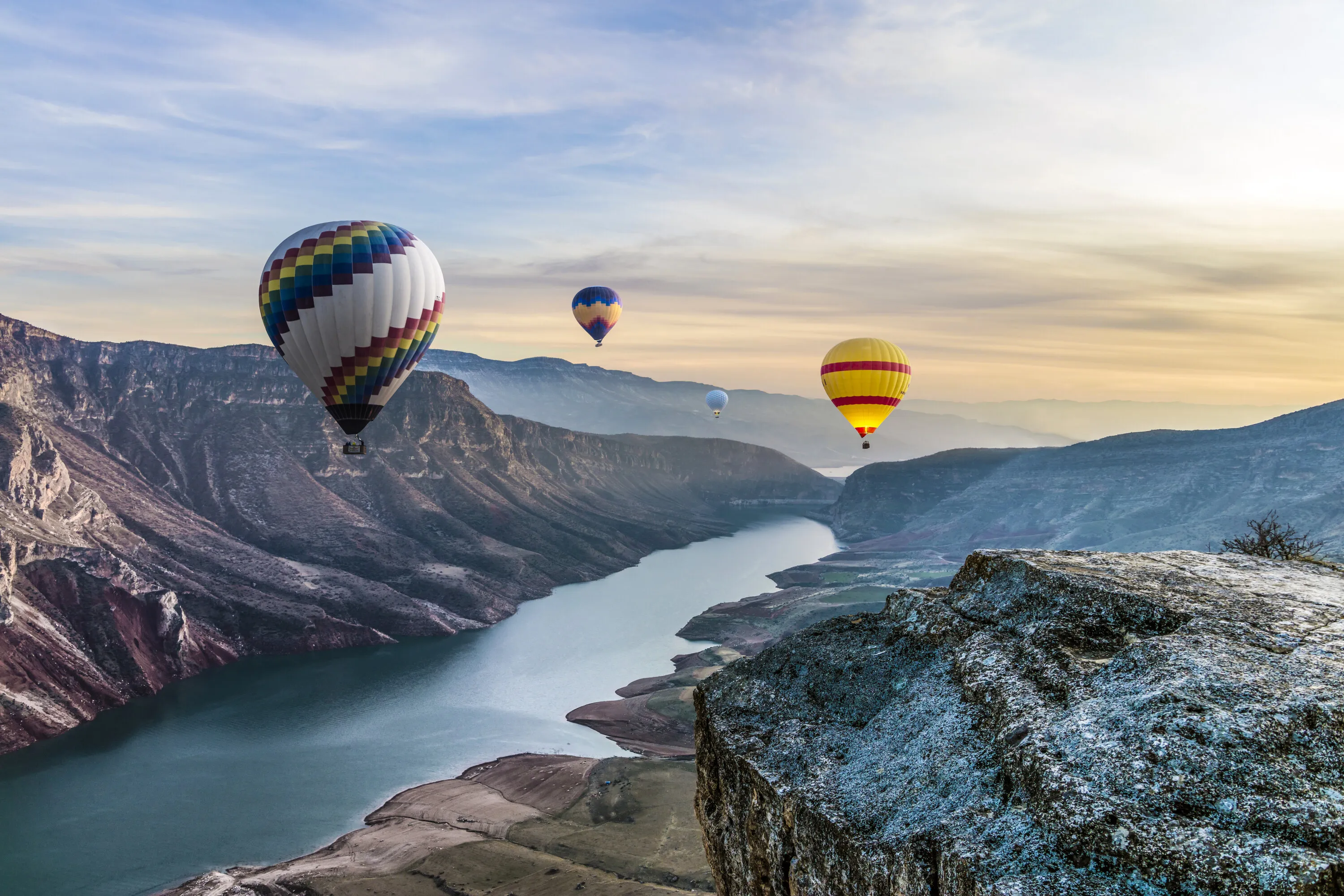Hot air balloons floating over a scenic canyon and river valley.